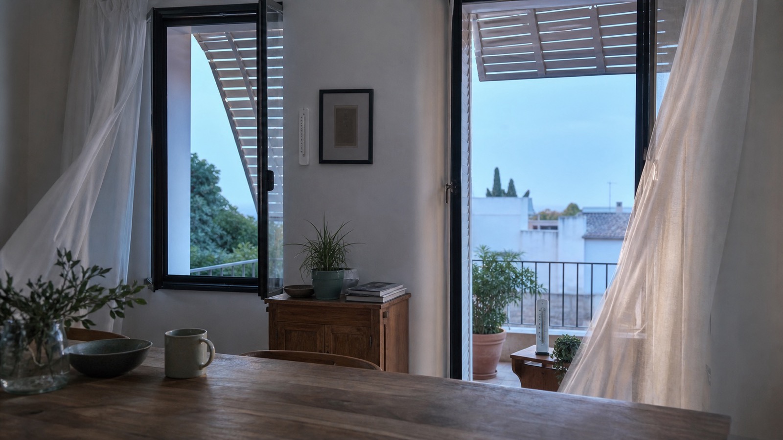 Estancia con dos huecos abiertos y cortinas movidas por una corriente suave al amanecer