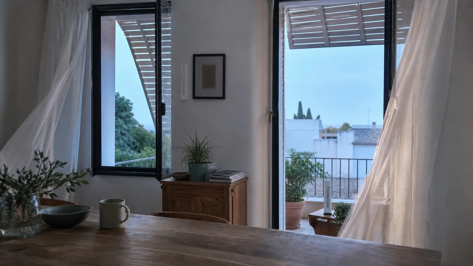 Ilustración: estancia con dos huecos abiertos y cortinas movidas por una corriente suave al amanecer